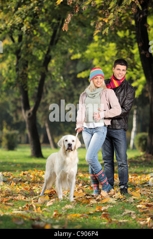 Una pareja sonriente y su perro posando en el parque en otoño
