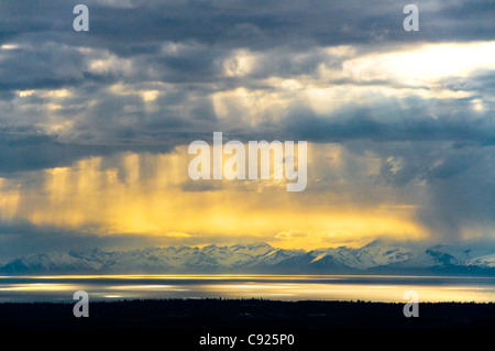 Resplandores de peek a través de las nubes a lo largo de la ensenada Cook, con el Chigmit Mountains, en el fondo, la Península Kenai, Alaska, muelle Foto de stock