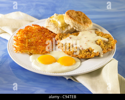 Filete de pollo frito con salsa servido con dos huevos, hash browns y galleta y mantequilla. Foto de stock