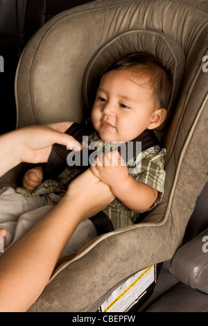 Sonriendo birracial Asiáticos Filipinos chico sentado en el asiento del coche mientras él hebilla de manos de padres Foto de stock