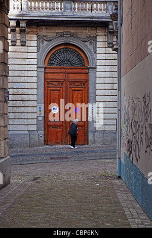 Solo anciana pasando la puerta de aspecto oficial en Bruselas - vista del callejón.