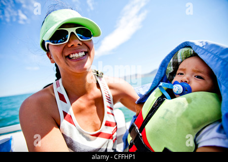 Una mujer nipo-estadounidenses en sus treinta sonríe mientras llevaba una visera verde espuma de costura, mientras mantiene su 7 mes de edad baby boy Foto de stock