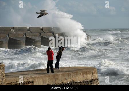 Contra el viento permanente dos personas ver olas masivas crash sobre Brighton Marina arm Foto de stock