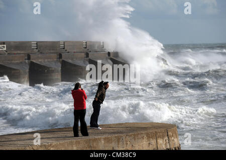 Contra el viento permanente dos personas ver olas masivas crash sobre Brighton Marina arm Foto de stock