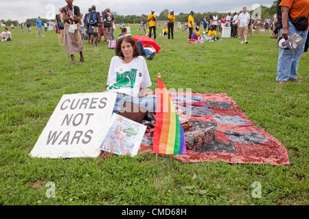 Una mujer descansa mientras muestra un signo y una bandera del arco iris, mientras espera para el SIDA de marzo en Washington, DC para iniciar - Julio 22, 2012, Washington, DC, EE.UU. Foto de stock