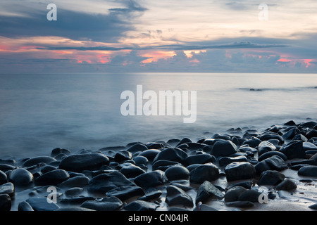 Olas rompiendo rocas en la playa de guijarros en la madrugada, cerca de Cairns, Queensland, Australia Foto de stock