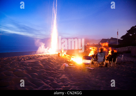 La gente en la playa con fogata y fuegos artificiales por la noche Foto de stock