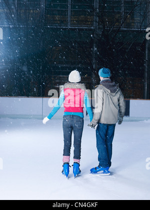 Las manos de la pareja en la pista de hielo, viendo la nieve caer Foto de stock