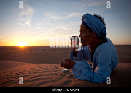 Nómada bereber beber té al atardecer en el desierto del Sáhara, Erg Chigaga, Marruecos Foto de stock