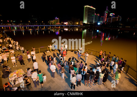 La población china local a orillas del río Wulie a cantar canciones tradicionales con las luces de Chengde en el fondo. Foto de stock