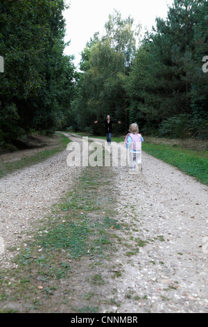 Bebé niña corriendo a la madre en el país por carretera, Farnham, Inglaterra Foto de stock