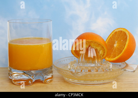 Zumo de naranja recién exprimido en un vaso con una licuadora y naranjas en una junta contra un fondo de cielo azul Foto de stock