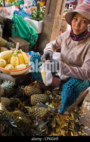 Vista vertical de una pobre señora vietnamita preparar piñas para venta en un alimento tradicional y el mercado de flores en la ciudad antigua de Hoi An, Vietnam. Foto de stock