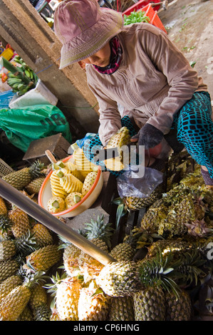 Vista vertical de una pobre señora vietnamita preparar piñas para venta en un alimento tradicional y el mercado de flores en la ciudad antigua de Hoi An, Vietnam. Foto de stock