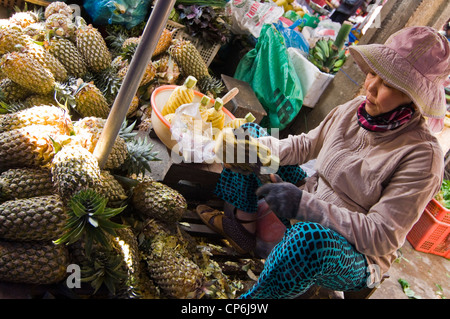 Vista horizontal de una pobre señora vietnamita preparar piñas para venta en un mercado de flores y alimentos tradicionales en Hoi An, Vietnam. Foto de stock