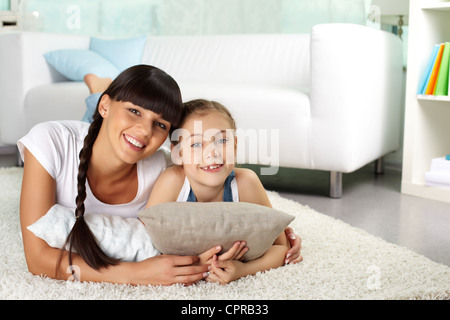 Retrato de niña alegre y su madre mirando a la cámara mientras descansa en casa