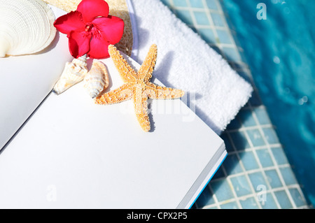 Libro Abierto, mariscos y toalla blanca junto a una piscina Foto de stock