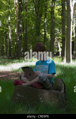 Hijo sentado en el bosque jugando con un iPad Foto de stock