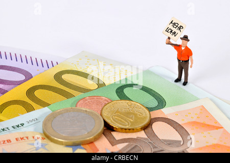 Un cartel de figurillas en miniatura, Mehr Lohn, Alemán para pagar más, junto a los billetes y monedas en euros