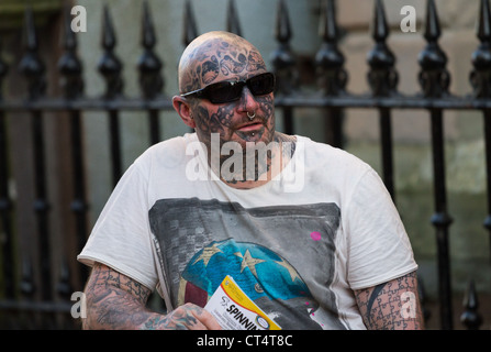 Un hombre fuertemente tatuado en la calle, con la cabeza rapada y gafas de sol. Foto de stock