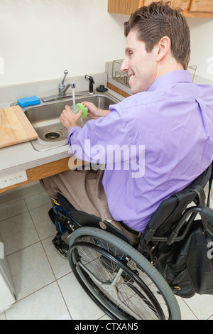 Hombre en silla de ruedas con lesión de la médula espinal de vidrio lavado en un fregadero accesible Foto de stock