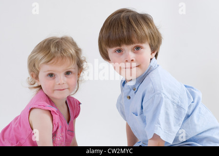 Joven y hermana de bebé en cuclillas junto con la cabeza girada mirando hacia la cámara, Studio retrato aislado en blanco