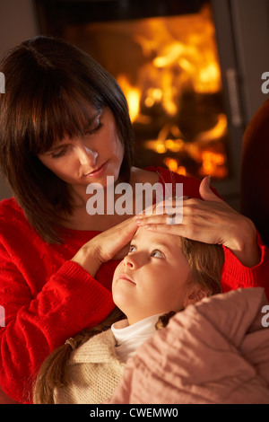 Madre reconfortante hija enferma en el sofá por un acogedor fuego de leña