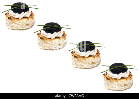 Canapés de caviar rojo y negro decorado con cebollino, sobre fondo blanco.