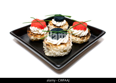 Canapés de caviar rojo y negro decorado con cebollino, sobre fondo blanco.