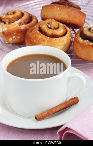 Una taza de café con bollos de canela recién horneados Foto de stock