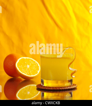 Zumo de naranja recién exprimido en el vaso con cáscara de naranja y naranjas sobre fondo naranja (enfoque selectivo) Foto de stock