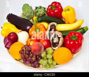 Un cesto de mimbre lleno de diversas frutas y verduras sobre un fondo blanco. Foto de stock
