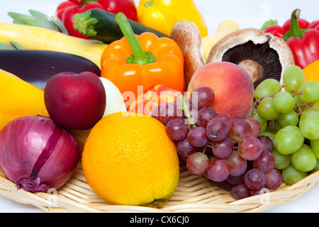 Un cesto de mimbre lleno de diversas frutas y verduras sobre un fondo blanco. Foto de stock