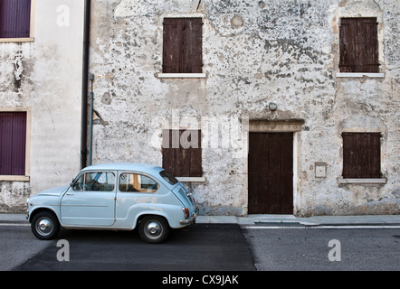 Un antiguo Fiat 500 coche frente a la fachada desmoronante de una casa antigua en el Veneto, Italia Foto de stock