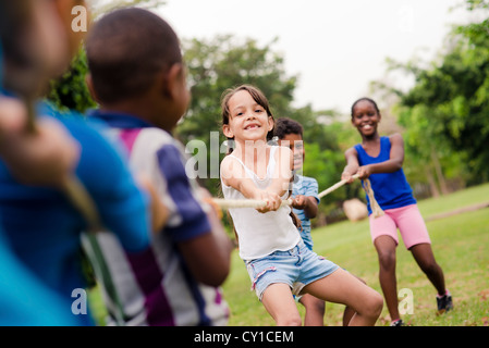 Los niños y la recreación, el grupo de niños de escuela multiétnica feliz jugando tug-of-war con la cuerda en el parque de la ciudad. Campamento de verano divertido