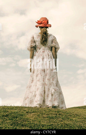 Una mujer en un vestido de flora y una red hat se está ejecutando en un prado Foto de stock