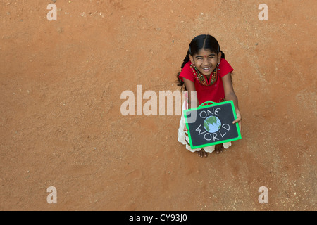 Indian Village chica con un mundo escrito en una pizarra en una aldea india. En Andhra Pradesh, India. Copie el espacio. Foto de stock