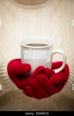 Mujer en un suéter rojo estacional mitones sosteniendo una taza de café caliente.