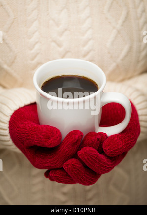 Mujer en un suéter rojo estacional mitones sosteniendo una taza de café caliente.