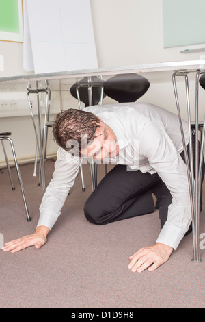 El hombre con la camisa blanca sentado debajo de la mesa en una oficina en busca de algo que se pierde.