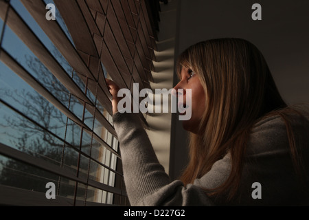 Ansiosa mujer madura mirando a través de las persianas de la ventana por la noche.