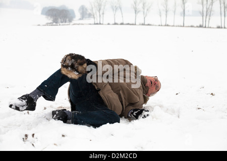 Hombre senior con pierna lesionada cayendo en la nieve. Foto de stock
