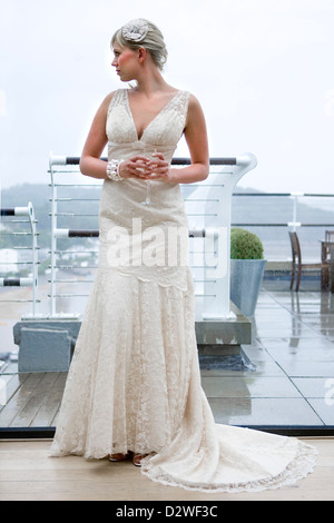 Una hermosa joven rubia novia mirando por una ventana mientras espera para su ceremonia de boda.