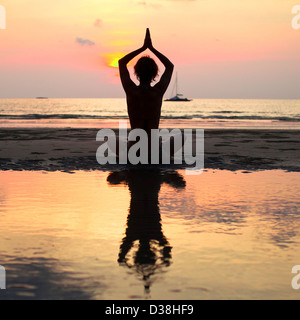 Yoga mujer sentada en lotus plantean en la playa durante la puesta de sol, con reflejo en el agua