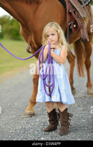 Poco chica rubia de pie junto a un gran caballo sujetando la línea de plomo. Foto de stock