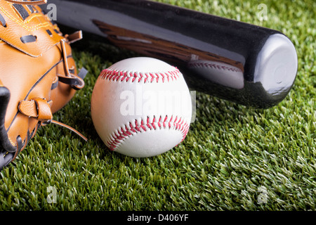 Una pelota de béisbol sobre la hierba verde con bat y guante Foto de stock