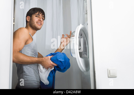 Hombre teniendo problemas en el funcionamiento de la lavadora en la lavandería del día Foto de stock