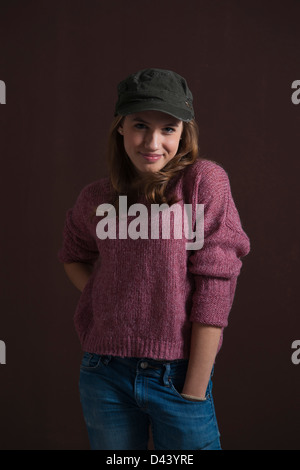 Retrato de una adolescente rubia, sonriendo a la cámara con la mano en el bolsillo llevar sombrero de béisbol, Foto de Estudio sobre fondo negro