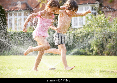 Dos niños corriendo a través de rociadores de jardín