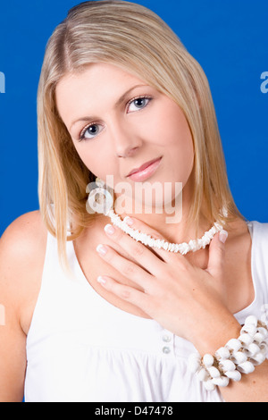 Una joven rubia bonita mujer caucásica con la cabeza inclinada y sosteniendo su collar de conchas. Foto de stock
